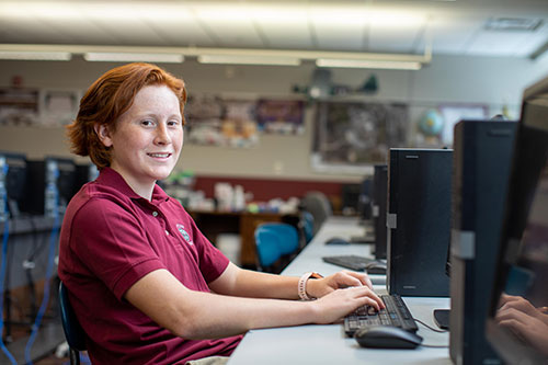 Male student sitting at desk reads braille to his teacher